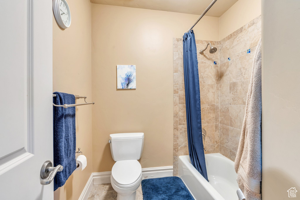 Full bathroom with toilet, shower / bath combo with shower curtain, and baseboards