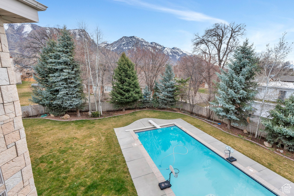 View of swimming pool featuring a fenced backyard, a lawn, a mountain view, and a diving board