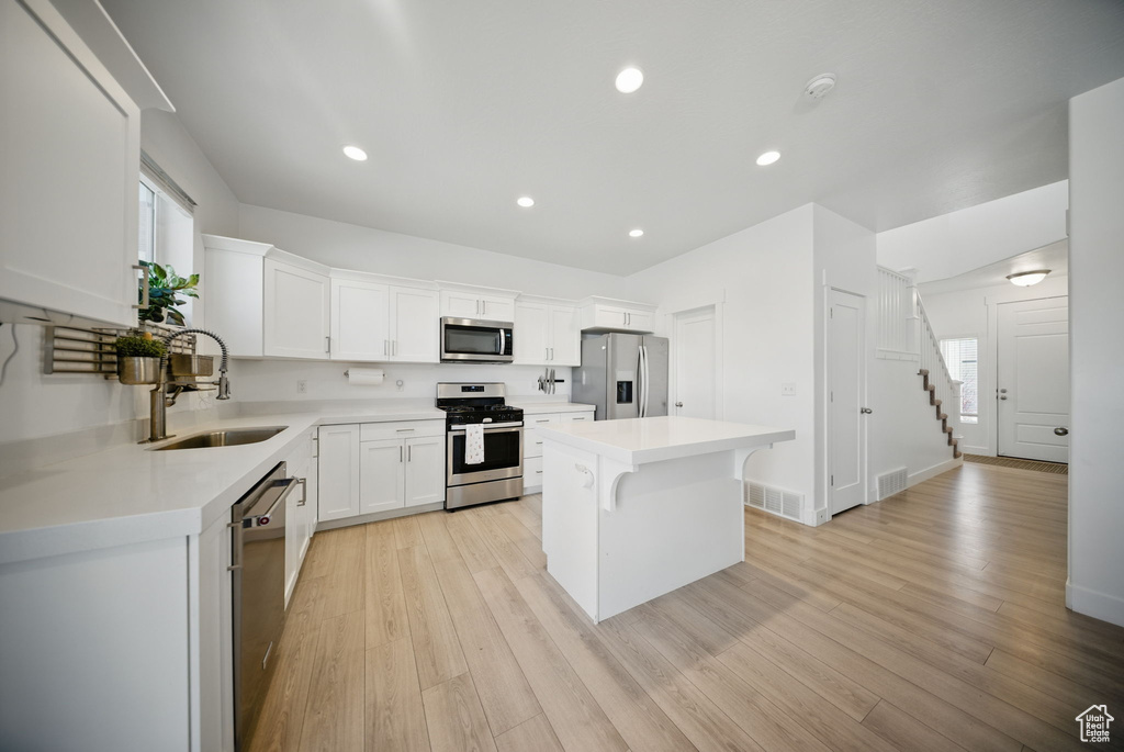 Kitchen with light wood-type flooring, a kitchen island, a sink, visible vents, and appliances with stainless steel finishes