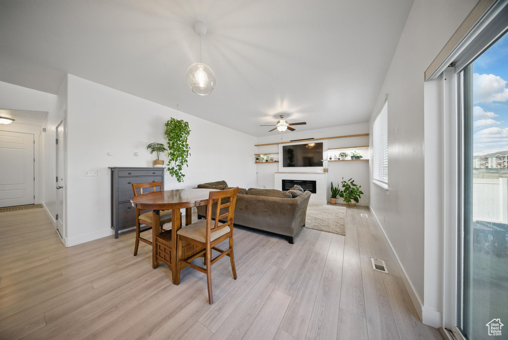 Dining space with visible vents, light wood-style flooring, ceiling fan, and a glass covered fireplace
