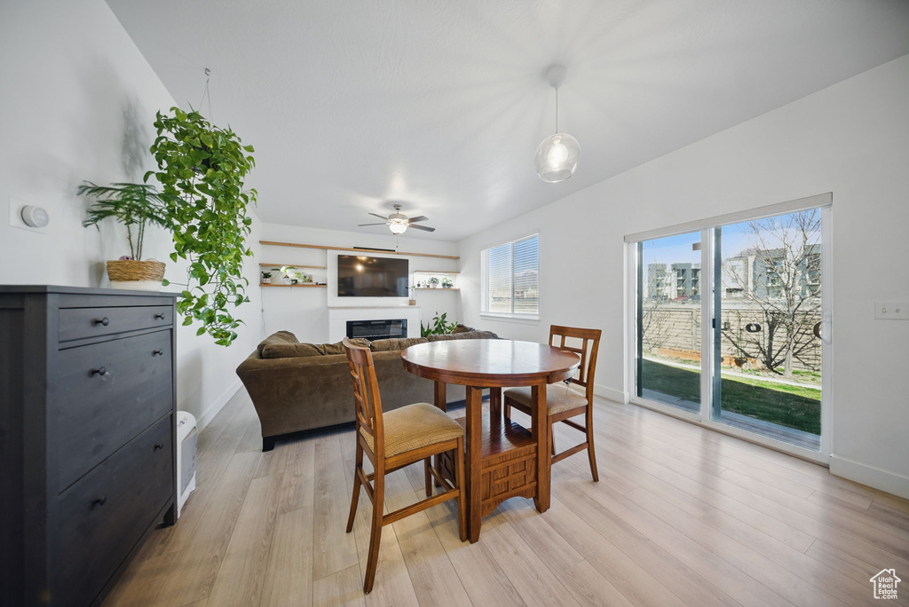 Dining space with baseboards, a glass covered fireplace, a ceiling fan, and light wood finished floors