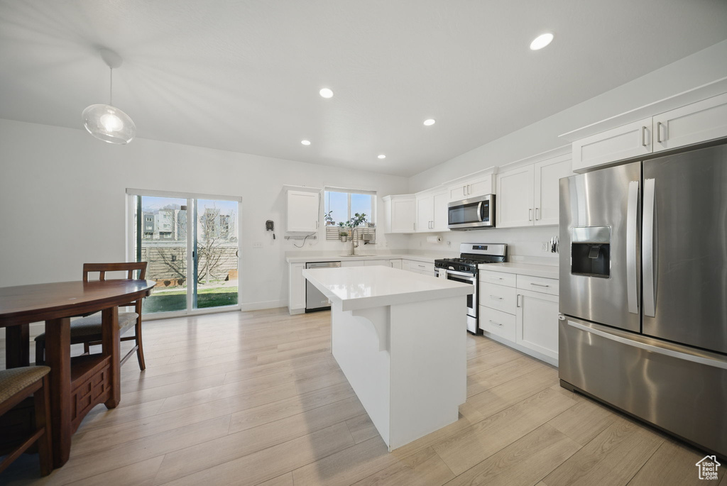 Kitchen with light countertops, light wood-style flooring, stainless steel appliances, white cabinetry, and a center island