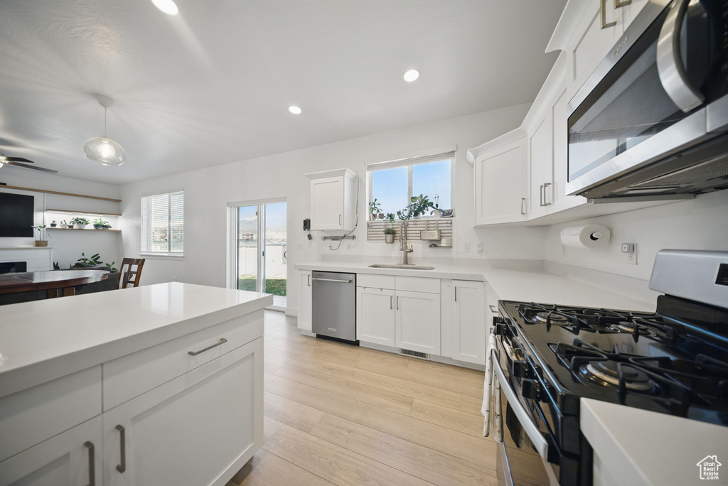 Kitchen with light countertops, light wood-style flooring, stainless steel appliances, white cabinetry, and a sink