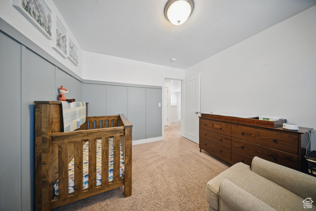 Carpeted bedroom featuring a wainscoted wall, a decorative wall, and a textured ceiling