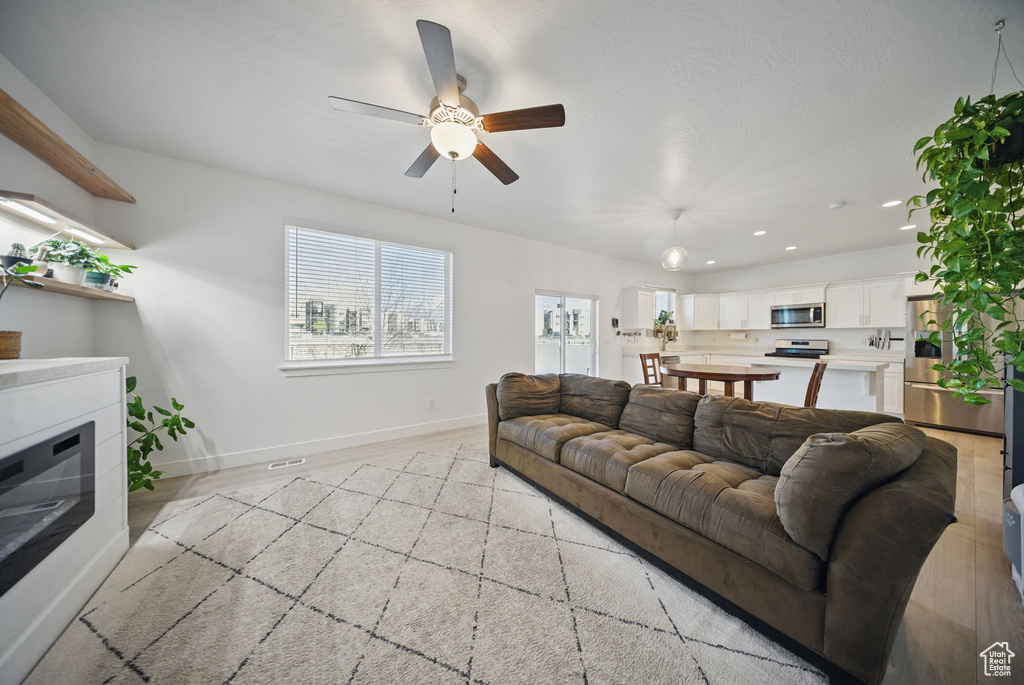 Living area with a glass covered fireplace, baseboards, light wood-style floors, ceiling fan, and recessed lighting