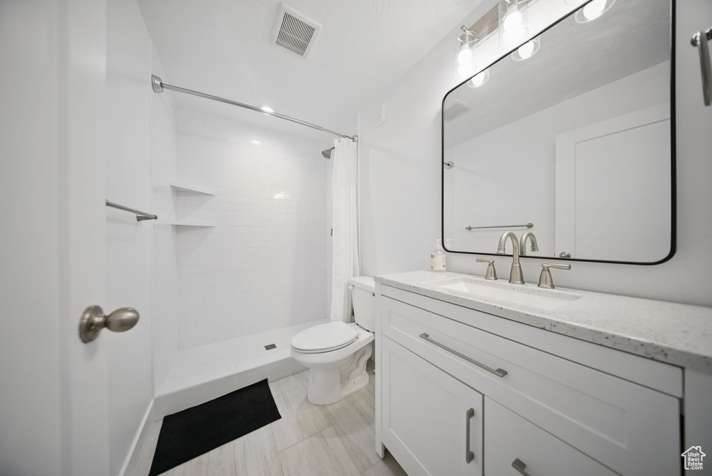 Full bathroom featuring tiled shower, visible vents, toilet, and vanity