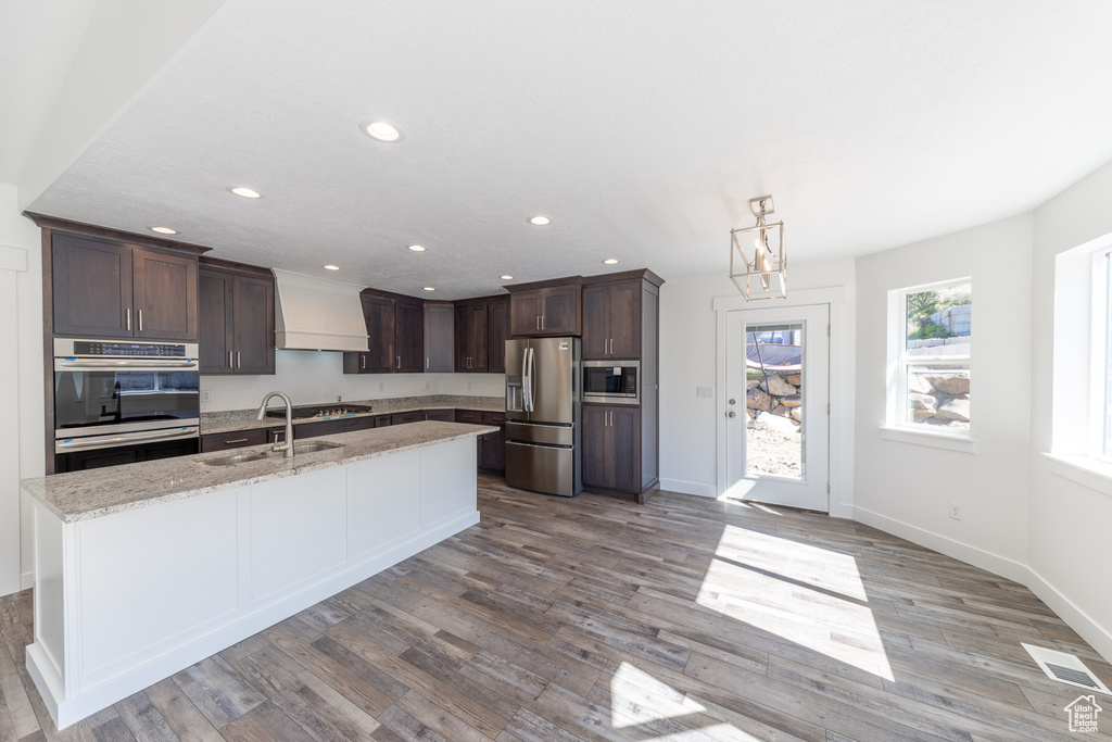 Kitchen featuring stainless steel appliances, a sink, premium range hood, dark brown cabinets, and recessed lighting