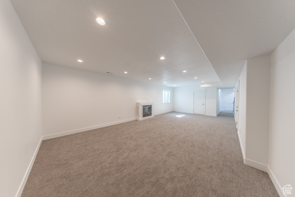 Unfurnished living room featuring carpet, recessed lighting, baseboards, and a glass covered fireplace