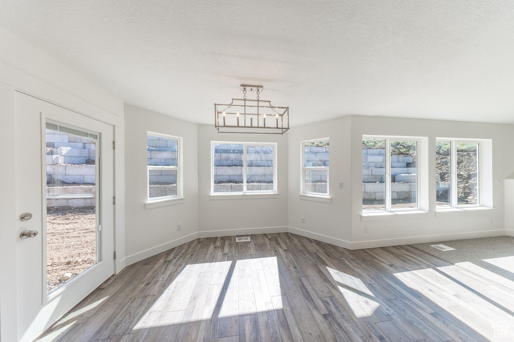 Unfurnished dining area with wood finished floors, a chandelier, and baseboards