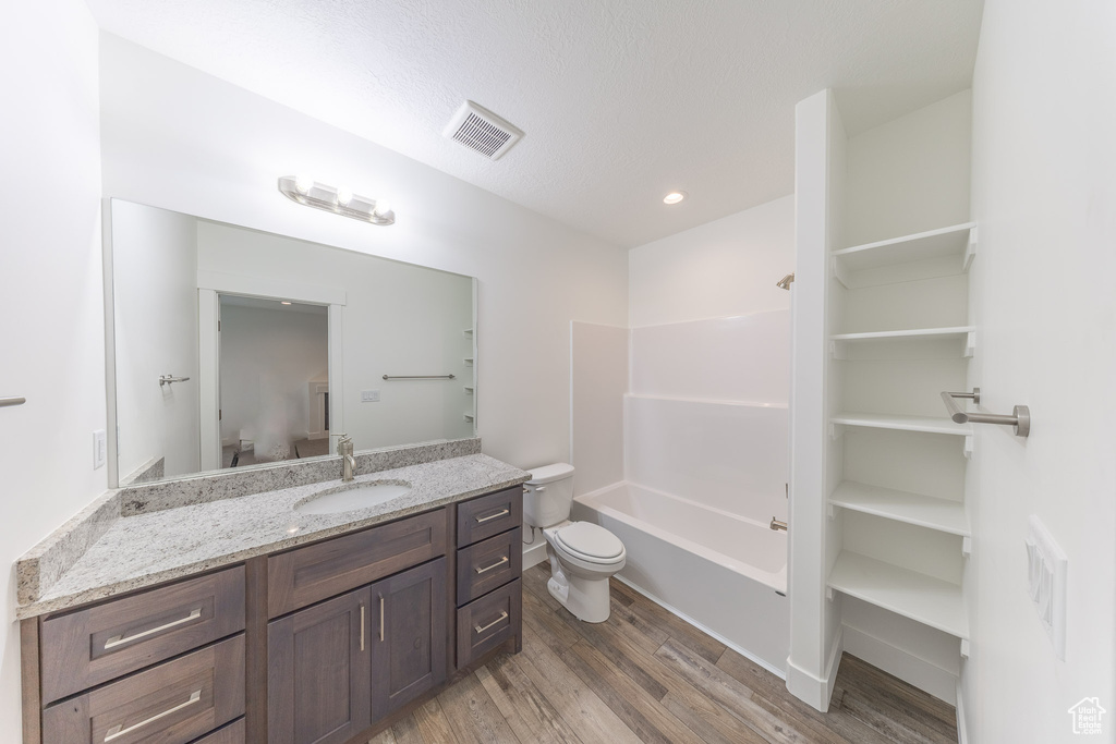 Bathroom with toilet, vanity, wood finished floors,  shower combination, and recessed lighting