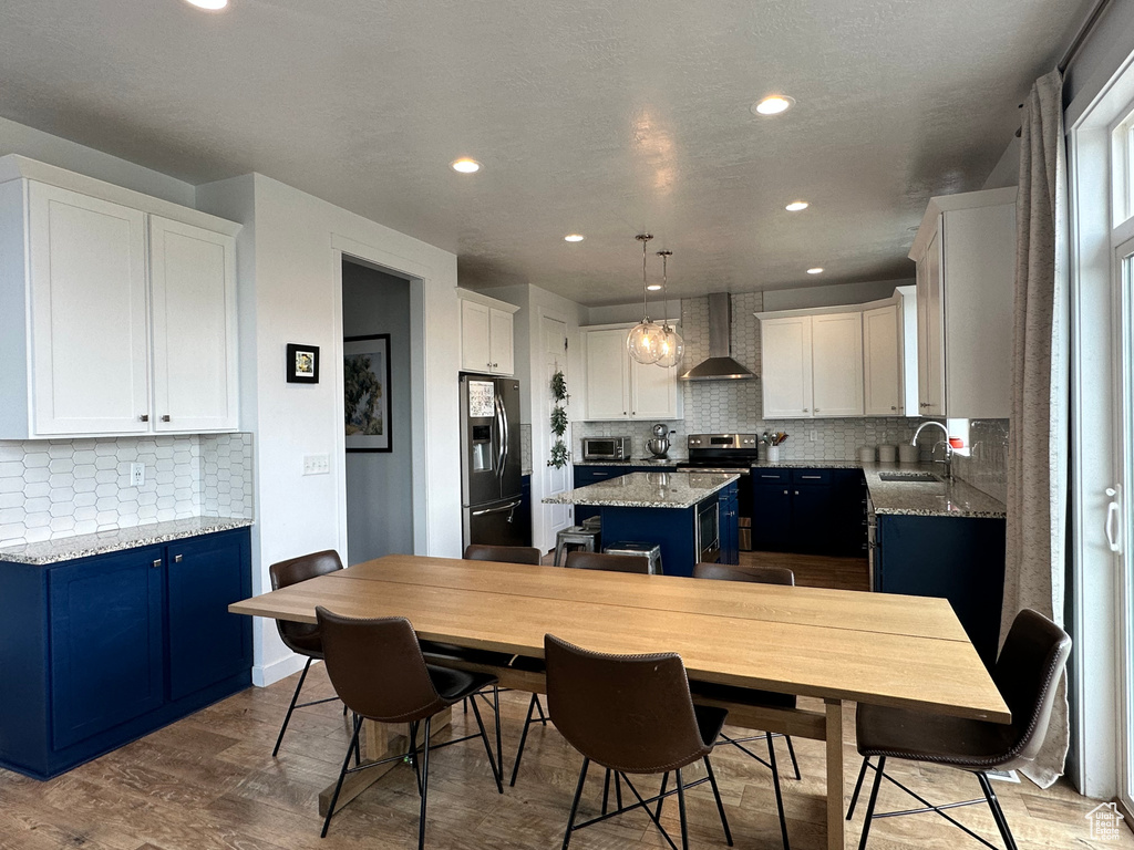 Kitchen featuring stainless steel appliances, wall chimney exhaust hood, blue cabinets, a sink, and a kitchen island
