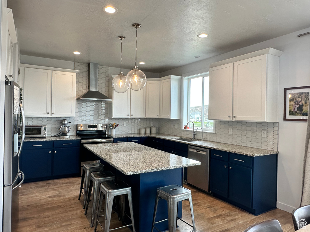Kitchen featuring wall chimney exhaust hood, appliances with stainless steel finishes, blue cabinets, a sink, and recessed lighting