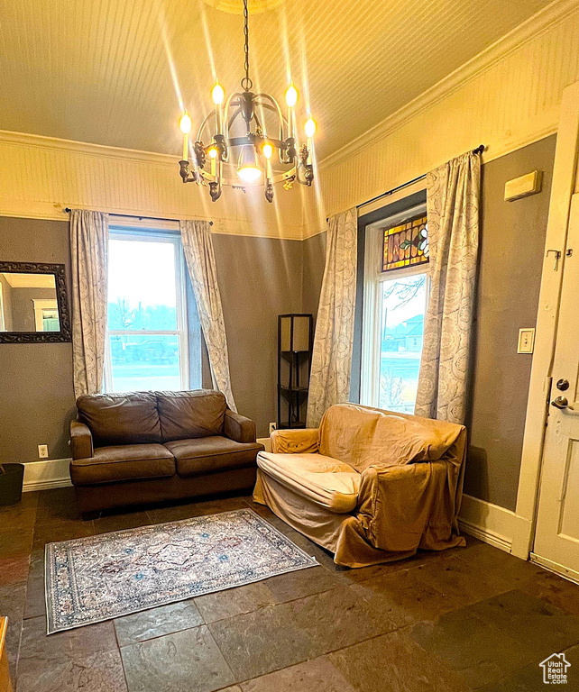 Living area featuring an inviting chandelier, stone tile floors, baseboards, and ornamental molding