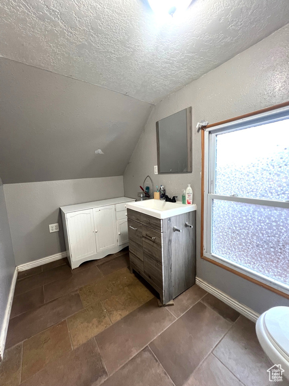 Bathroom featuring baseboards, a textured ceiling, lofted ceiling, and vanity