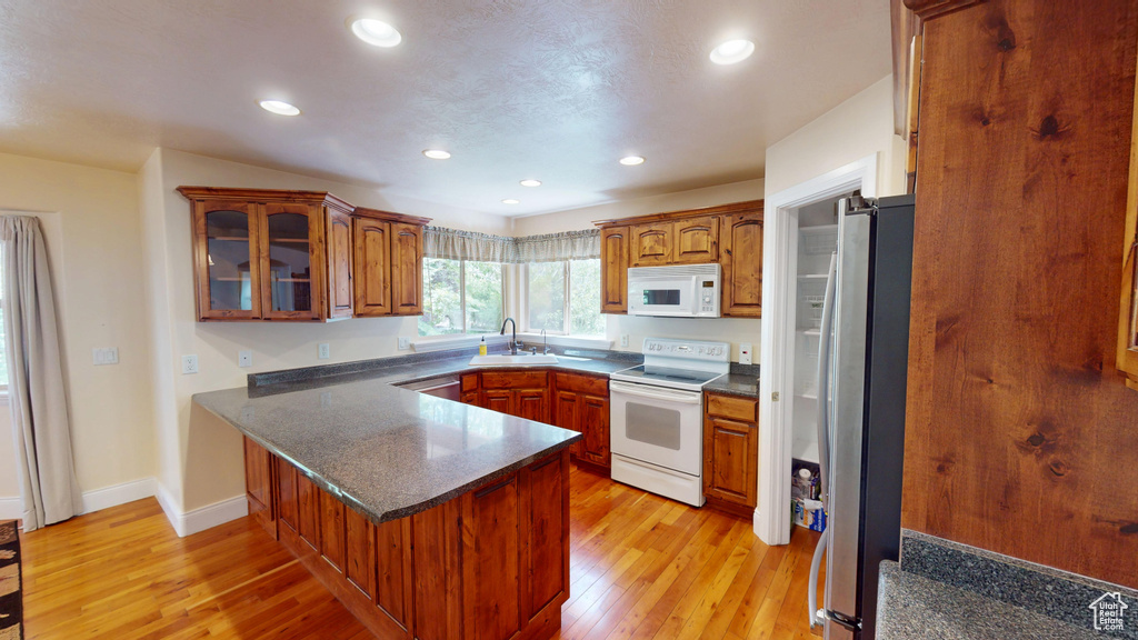Kitchen with appliances with stainless steel finishes, a peninsula, light wood-type flooring, glass insert cabinets, and recessed lighting