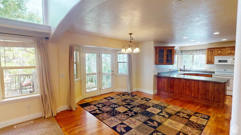 Kitchen featuring white appliances, a peninsula, a chandelier, light wood finished floors, and recessed lighting