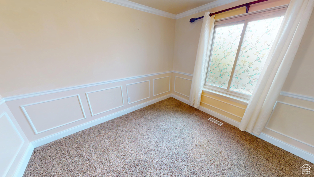 Unfurnished room featuring carpet, ornamental molding, a decorative wall, and wainscoting