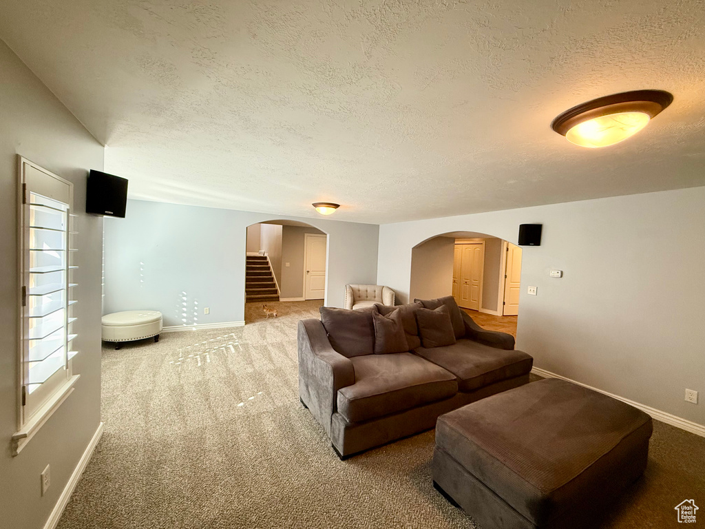Carpeted living room with arched walkways, baseboards, stairway, and a textured ceiling
