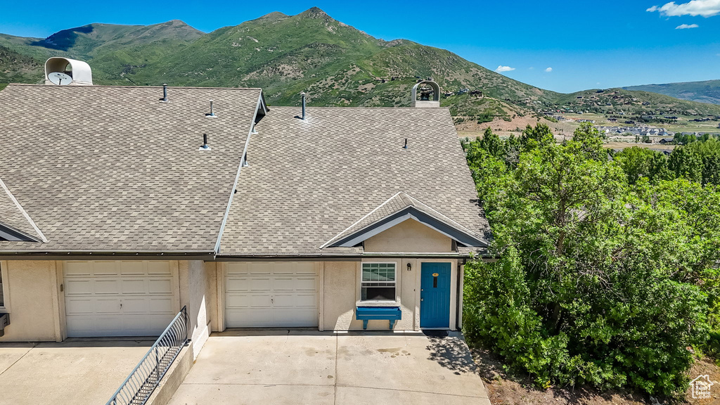 View of front facade with concrete driveway, a mountain view, a shingled roof, and stucco siding