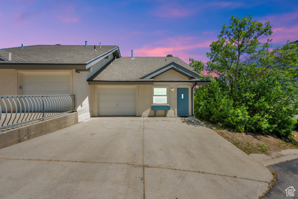 View of front facade featuring driveway, roof with shingles, an attached garage, and stucco siding