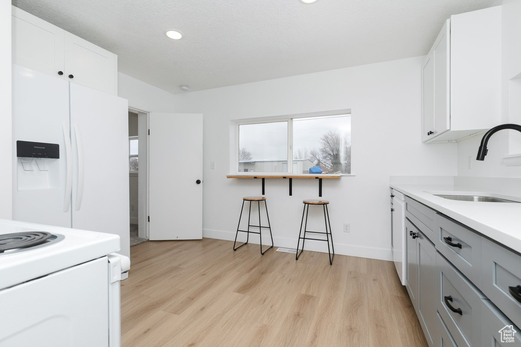 Kitchen with light countertops, a sink, light wood-type flooring, white appliances, and white cabinets