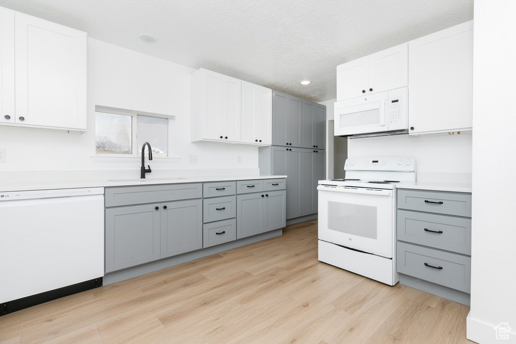 Kitchen with gray cabinets, light countertops, a sink, light wood-type flooring, and white appliances