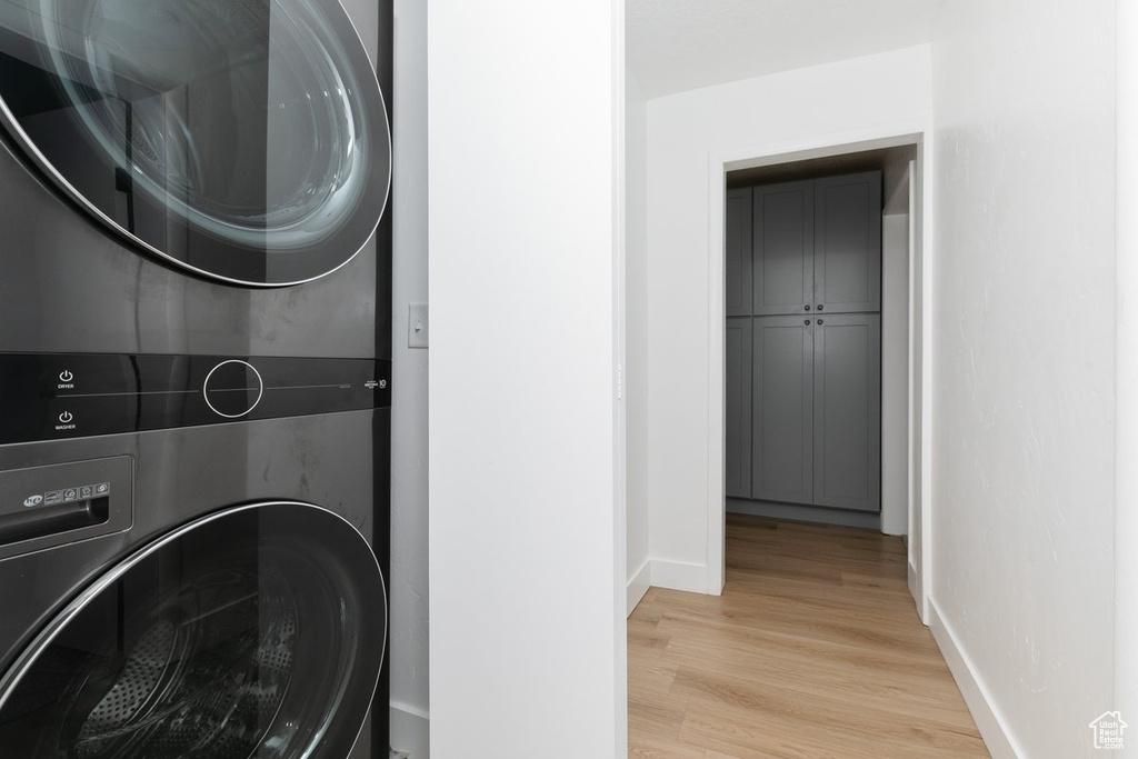 Washroom featuring light wood finished floors, baseboards, stacked washer and clothes dryer, and laundry area