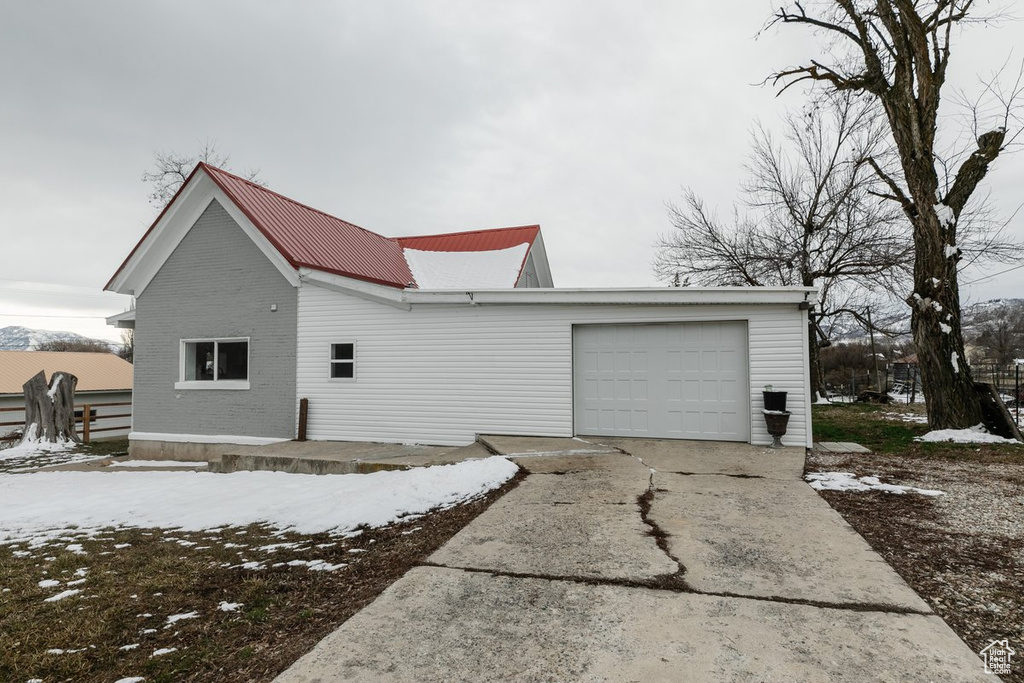View of snow covered exterior with driveway, a garage, and metal roof