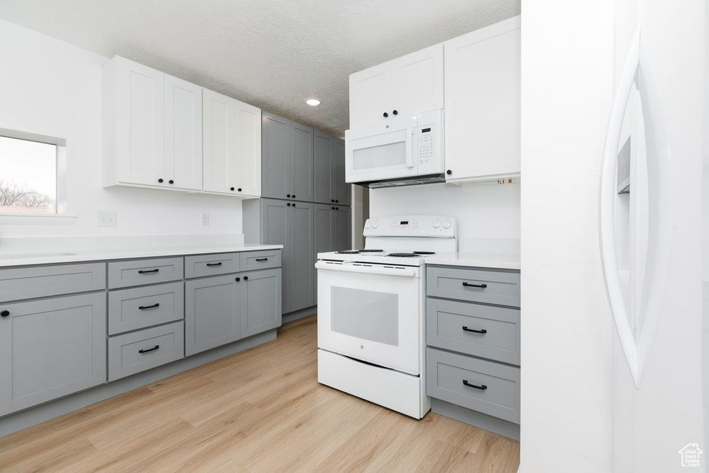 Kitchen featuring light countertops, white appliances, gray cabinetry, a sink, and light wood-style flooring