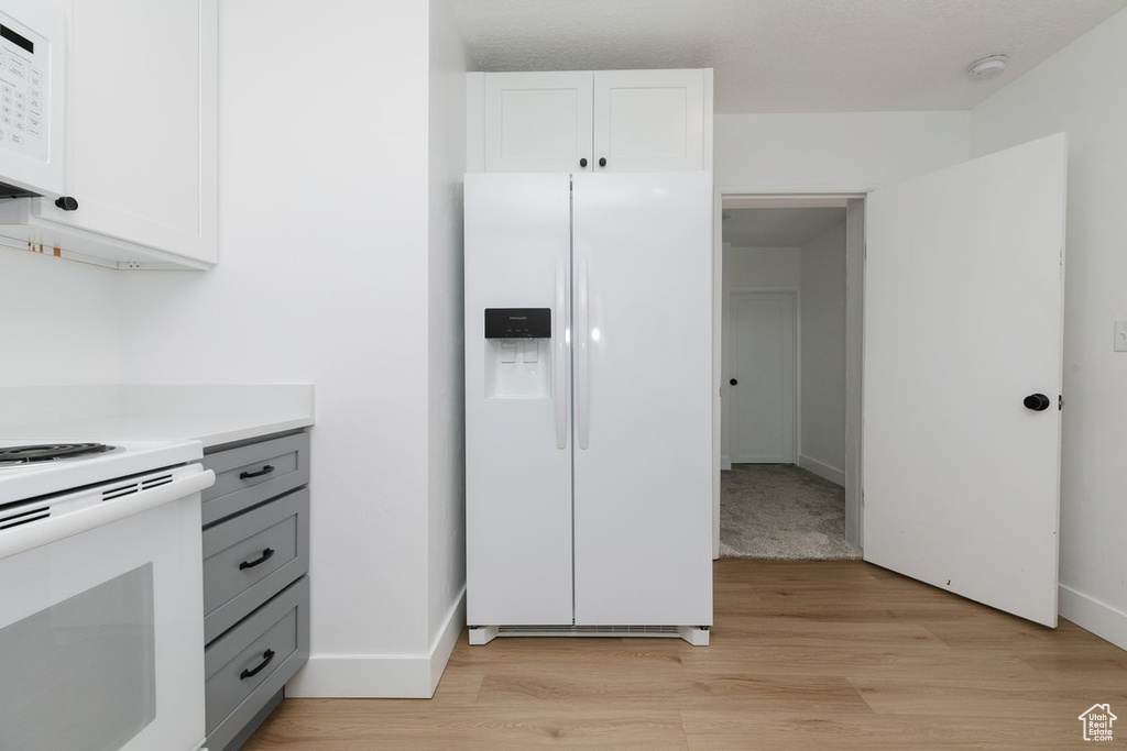 Kitchen featuring white appliances, light wood-type flooring, white cabinets, and light countertops