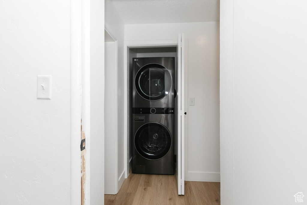 Washroom featuring light wood-style flooring, stacked washer / drying machine, and laundry area