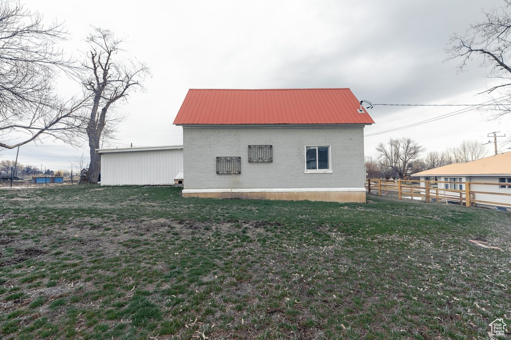 View of side of property with metal roof, fence, brick siding, and a yard