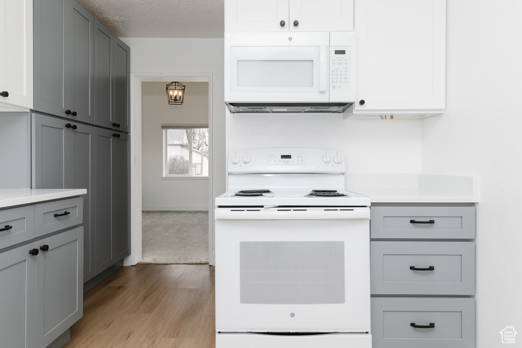 Kitchen featuring a textured ceiling, light countertops, white appliances, wood finished floors, and gray cabinetry