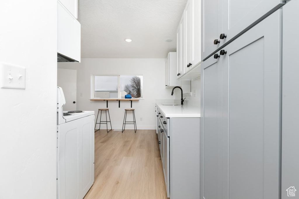 Kitchen featuring white cabinetry, light countertops, stove, a sink, and light wood finished floors