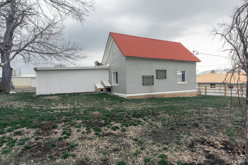 Back of house with metal roof, fence, brick siding, and a yard