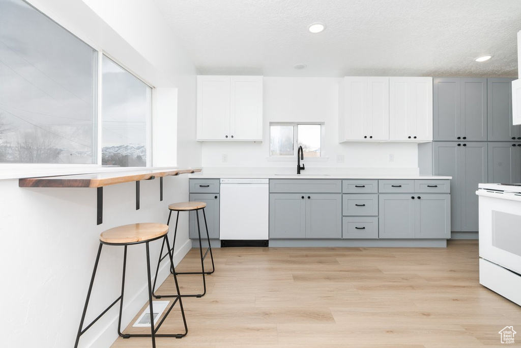 Kitchen featuring light countertops, light wood finished floors, white appliances, recessed lighting, and a sink