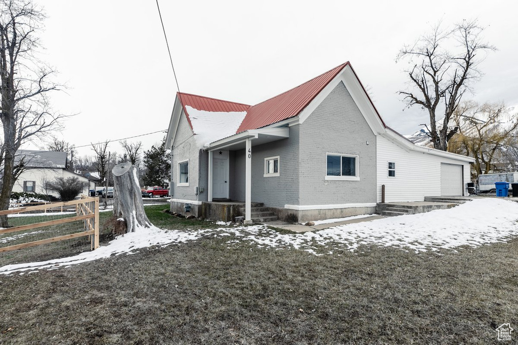 View of snowy exterior with metal roof, fence, and brick siding