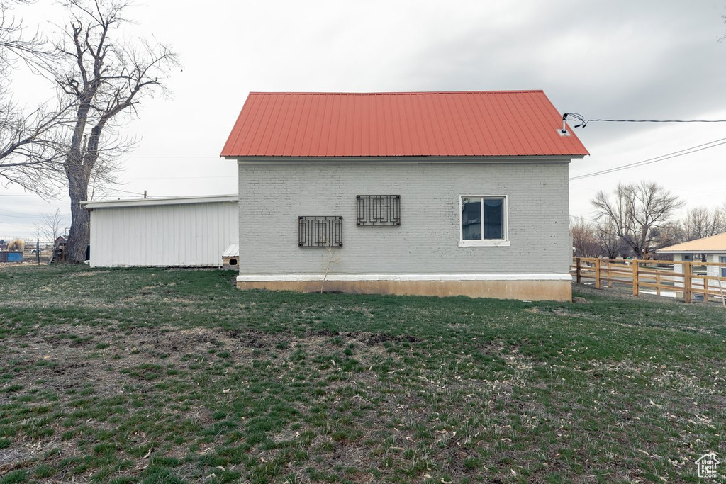 View of property exterior featuring a lawn, metal roof, fence, and brick siding