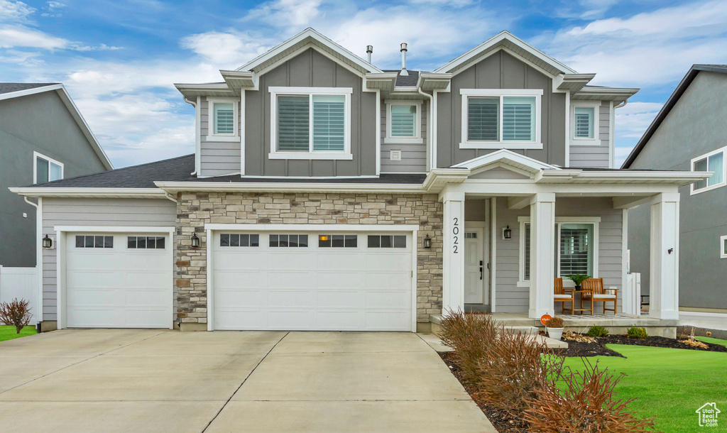 View of front of house with board and batten siding, covered porch, driveway, and stone siding