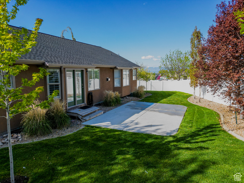 Back of property featuring a lawn, a patio area, fence, a shingled roof, and stucco siding