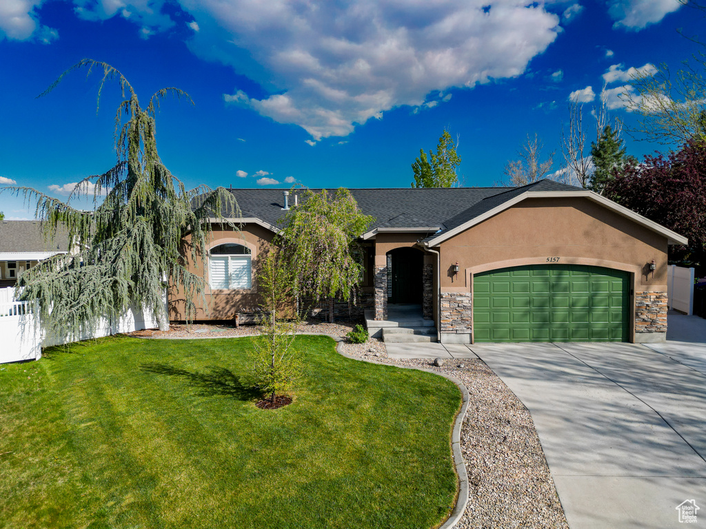 Ranch-style home featuring a front yard, concrete driveway, an attached garage, stone siding, and stucco siding