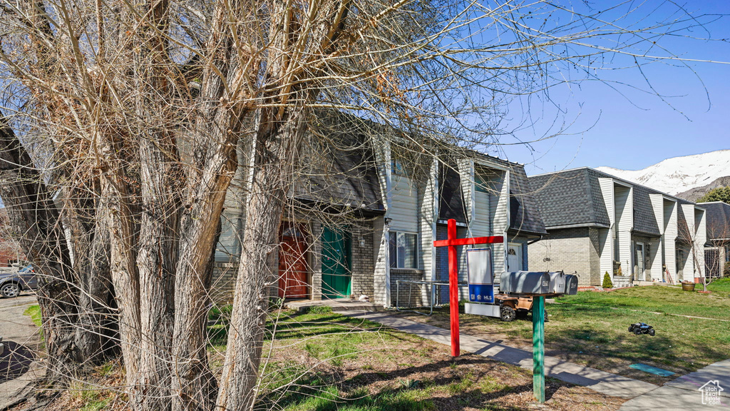 View of front of home with roof with shingles, mansard roof, brick siding, a front lawn, and a mountain view