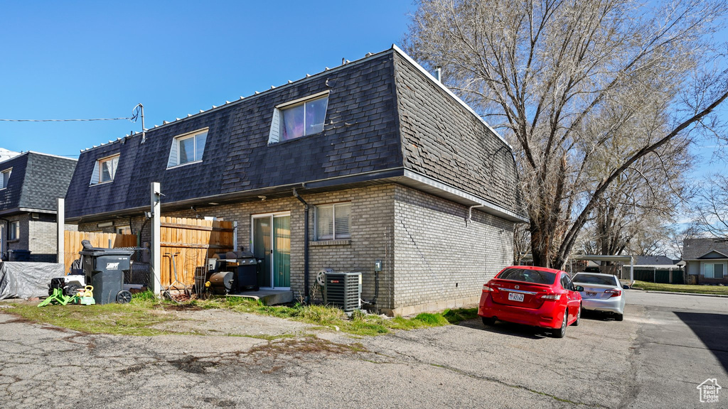 Exterior space with roof with shingles, fence, brick siding, mansard roof, and central AC