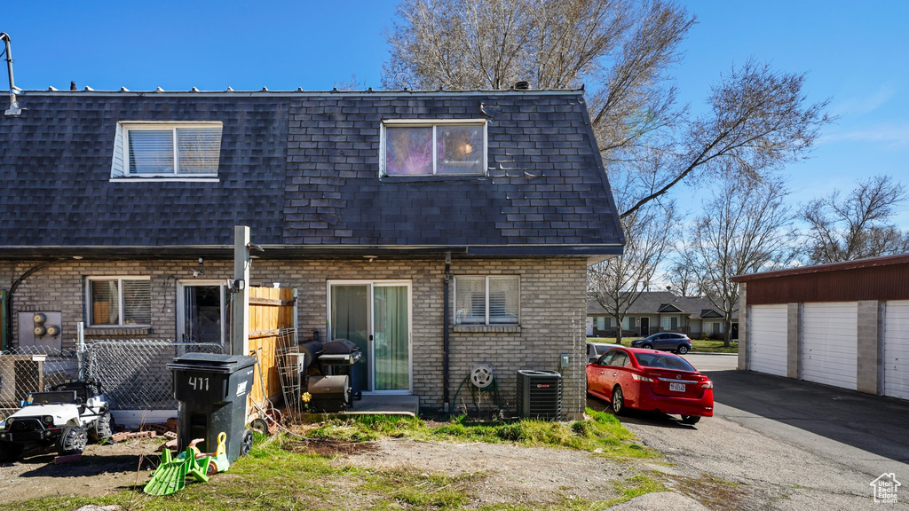Rear view of house with cooling unit, fence, mansard roof, brick siding, and a shingled roof