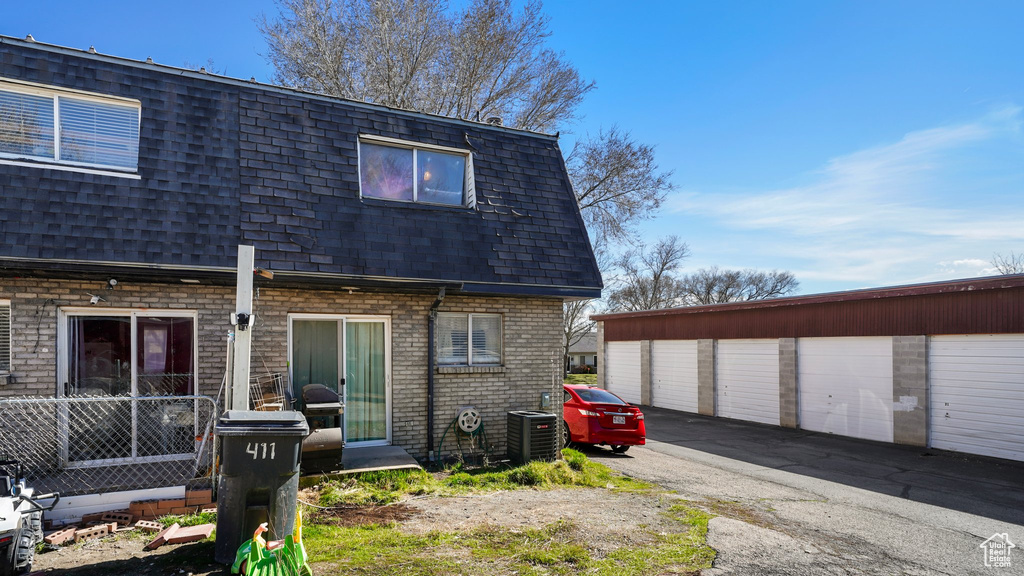 Rear view of property with central AC unit, brick siding, a shingled roof, and mansard roof