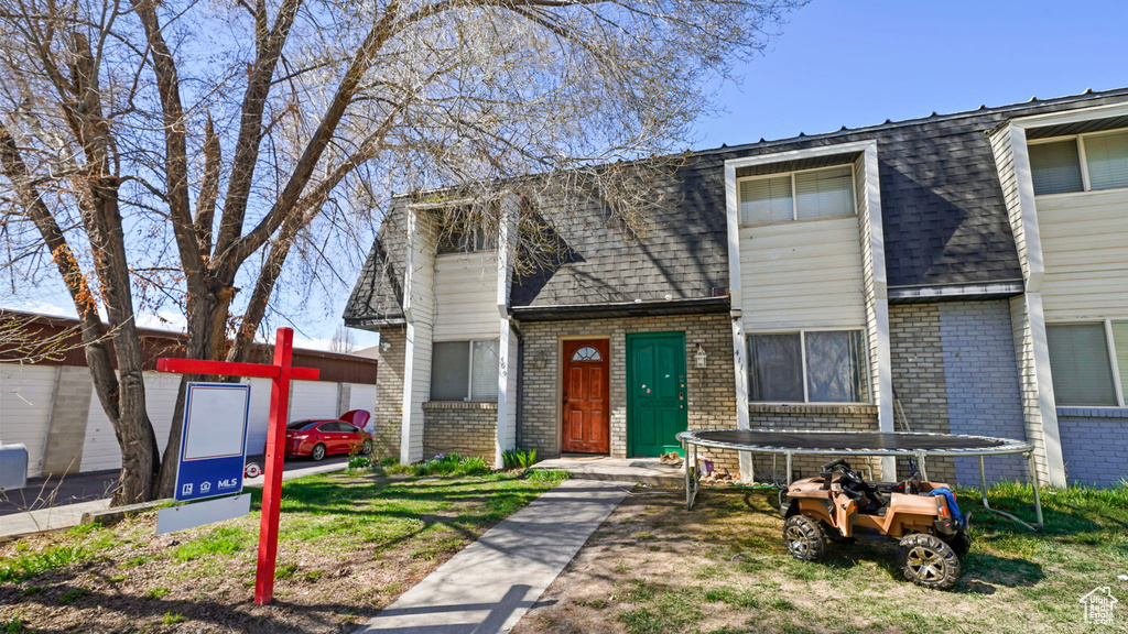 View of property featuring mansard roof, brick siding, and roof with shingles