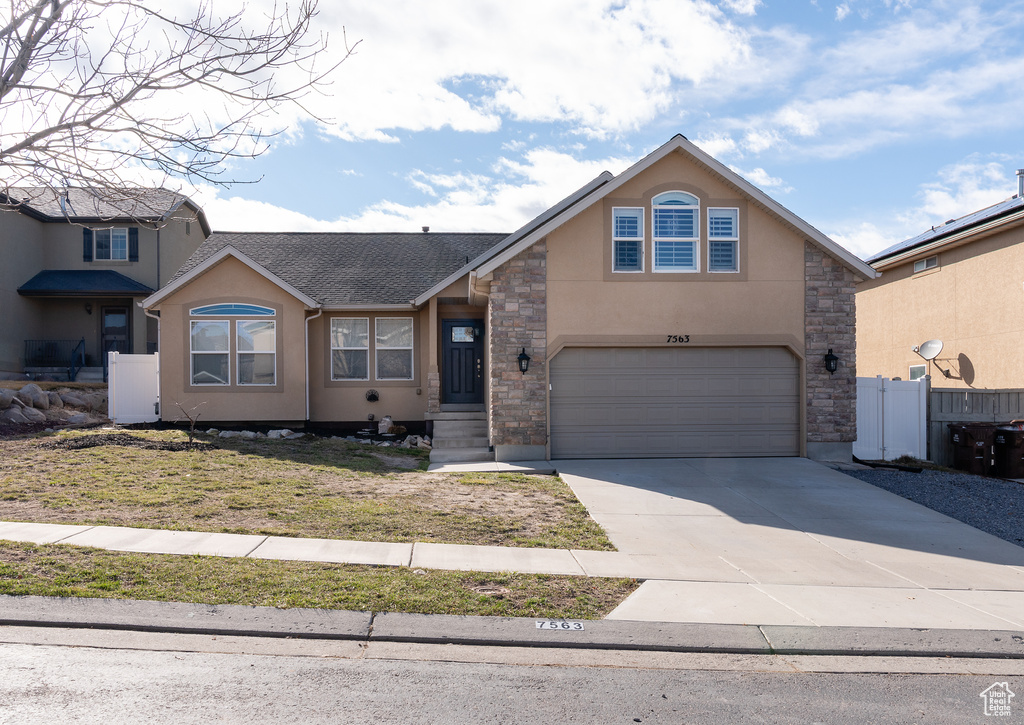 View of front of home with stone siding, driveway, fence, a garage, and stucco siding
