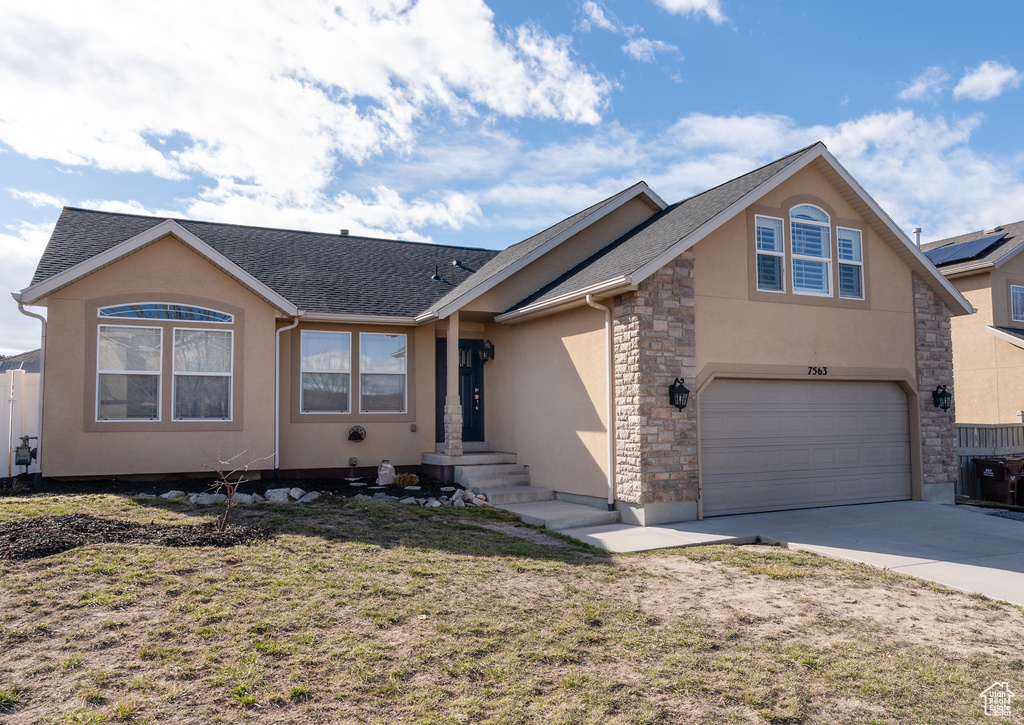 View of front facade with stone siding, concrete driveway, stucco siding, an attached garage, and a front lawn