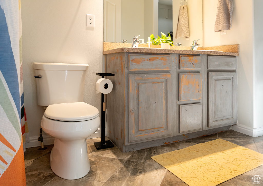Full bath with toilet, double vanity, a sink, and baseboards
