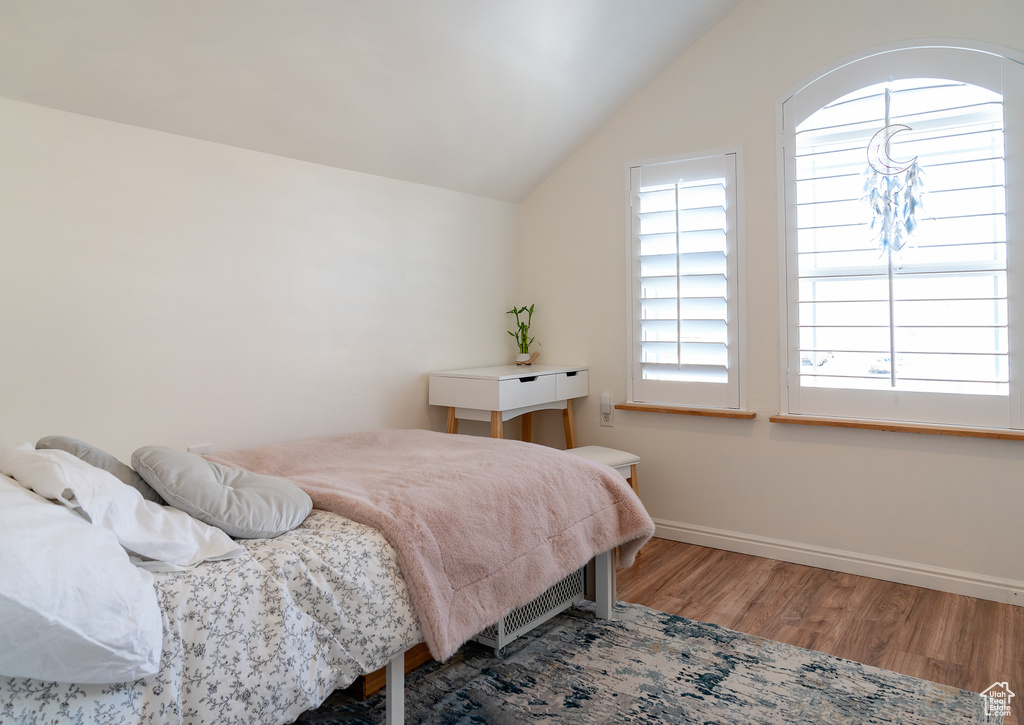 Bedroom with baseboards, lofted ceiling, wood finished floors, and multiple windows